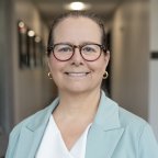 Sharon Kanfoush in a green blazer and red glasses, smiles at the camera.