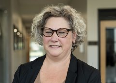 Trista Richardson in black blazer and red glasses, smiles at camera.