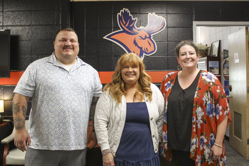 The Student Involvement and Leadership Team stand in front of a painted brick wall with an orange moose on it.